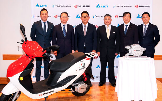 電動二輪車と駆動ユニットとともに、記念撮影する武蔵精密工業、デルタ、豊田通商の関係者（武蔵精密提供） 