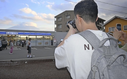 再設置された幕越しにコンビニと富士山を撮影する観光客＝14日、山梨県富士河口湖町（共同）