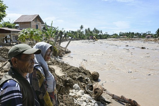 ２日、インドネシア西スマトラ州パダンで、自宅があった場所を流れる濁流を見つめるヘリヤンティさん（右）と夫（共同）