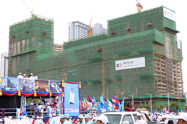 カンボジア人民党の支持者の背後で存在感を示す中国企業の看板＝７月上旬、プノンペン（ＮＮＡ撮影） 