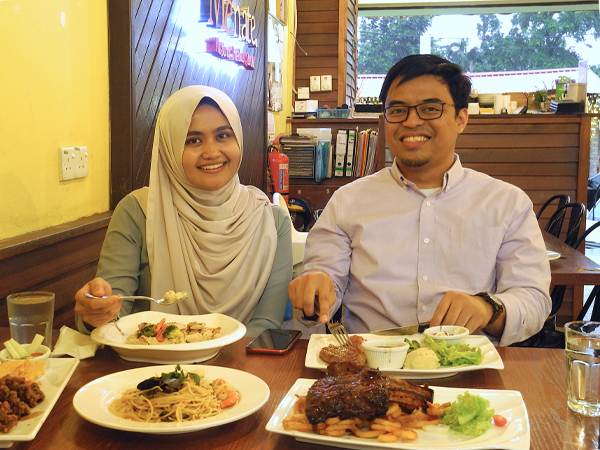 幸せいっぱいのファヒムさん（右）。ステーキを頬張りながら「ベンツに乗りたい」と夢を語る。妻のシャザさん（左）は「まだ早い。今ので充分」とたしなめる＝マレーシア・クアラルンプール（筆者撮影）