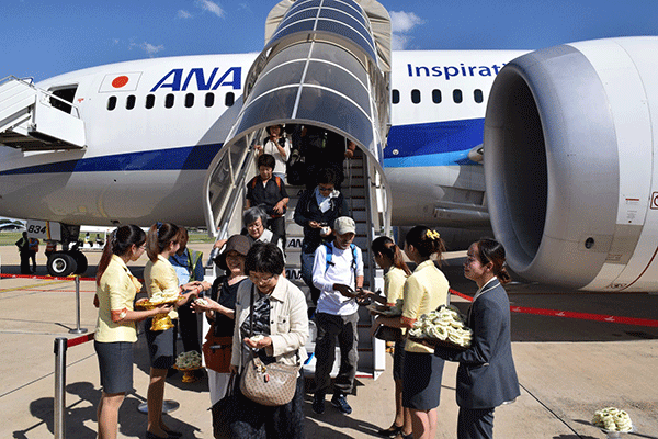 第１便の到着後に全日空の機体を降り、記念の花を受け取る搭乗者ら＝プノンペン（ＮＮＡ撮影）